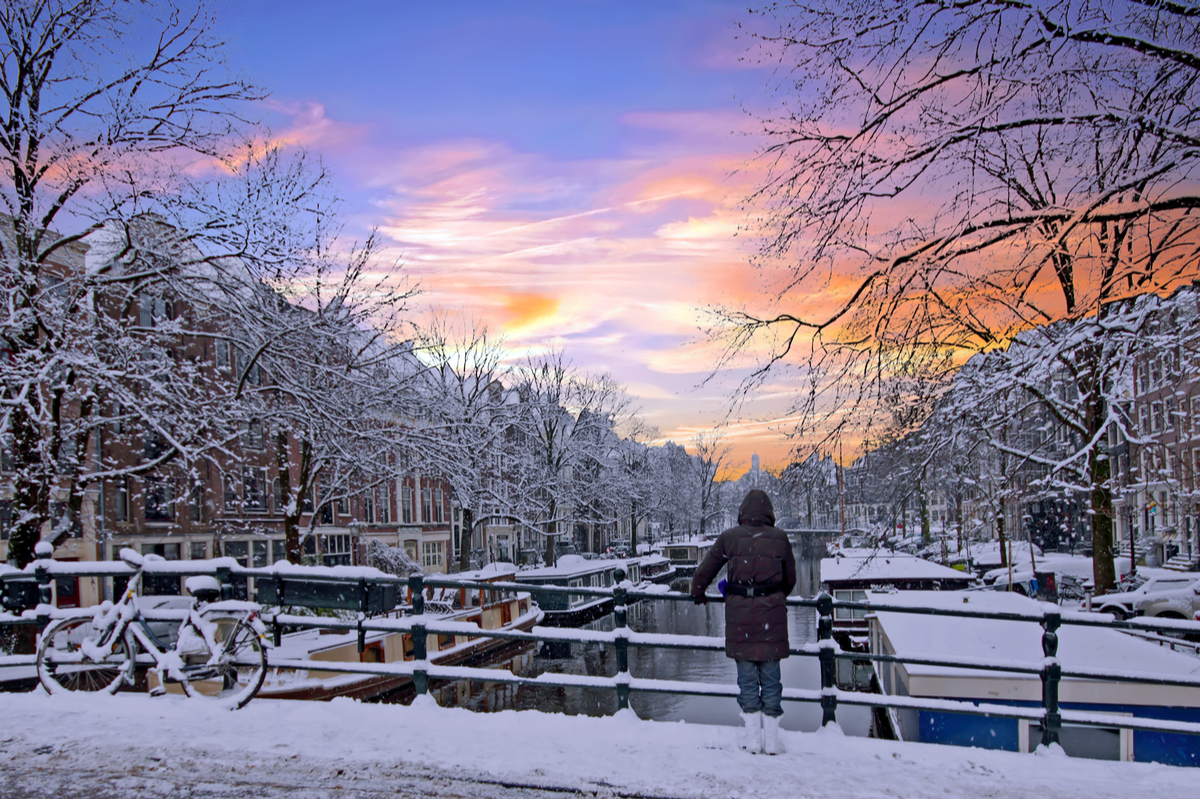 Woman standing on canal bridge in Amsterdam in winter snow