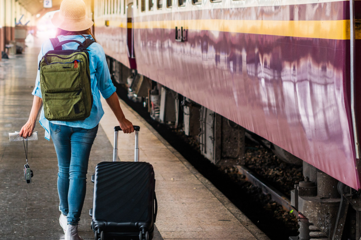 Female traveller with small suitcase on train platform rail tour